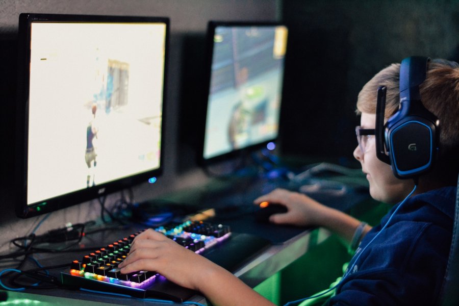 Ein Junge, der etwa 12 Jahre alt ist, spielt Fortnite. Er sitzt mit Headset vor einem großen Bildschirm.