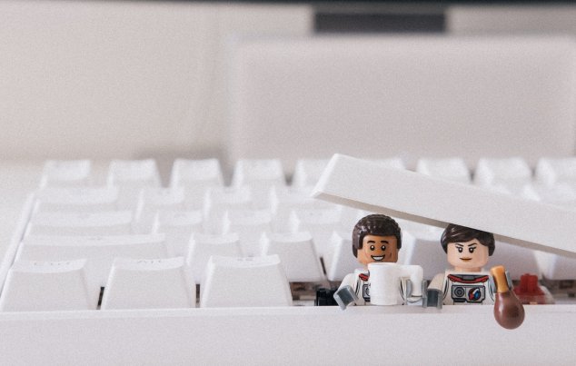 Zwei Lego-Figuren schauen aus einer weißen Tastatur heraus.