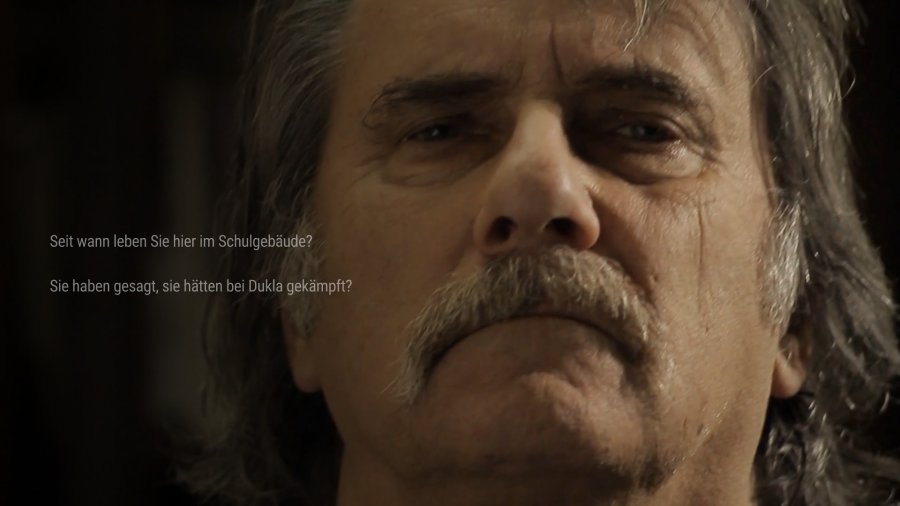 Ein älterer Mann mit grauem Schnauzbart und langen grauen Haaren schaut ernst in die Kamera. Links neben seinem Gesicht erscheinen Dialogoptionen.