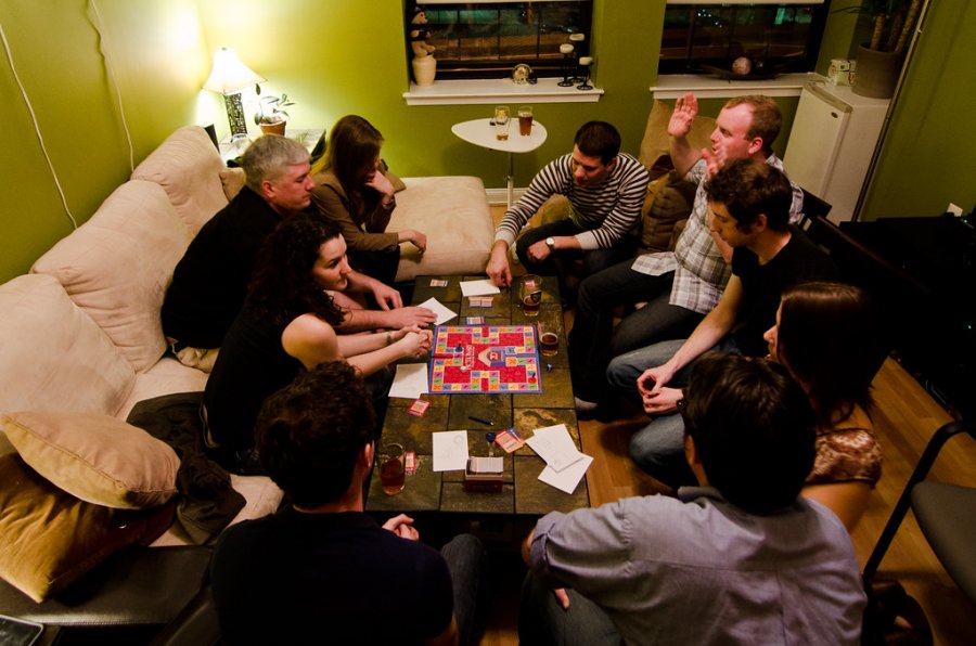 eine Spielrunde, ein Spieleabend mit sechs bis acht Personen mittleren Alters an einem Tisch. Ein Brettspiel.
