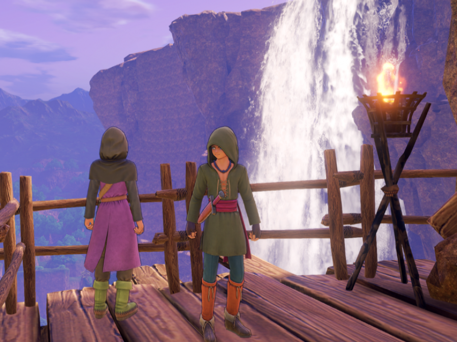 Zwei Personen stehen auf einem Hölzernen Boden mit Geländer. Im Hintergrund ist ein Wasserfall zu sehen.