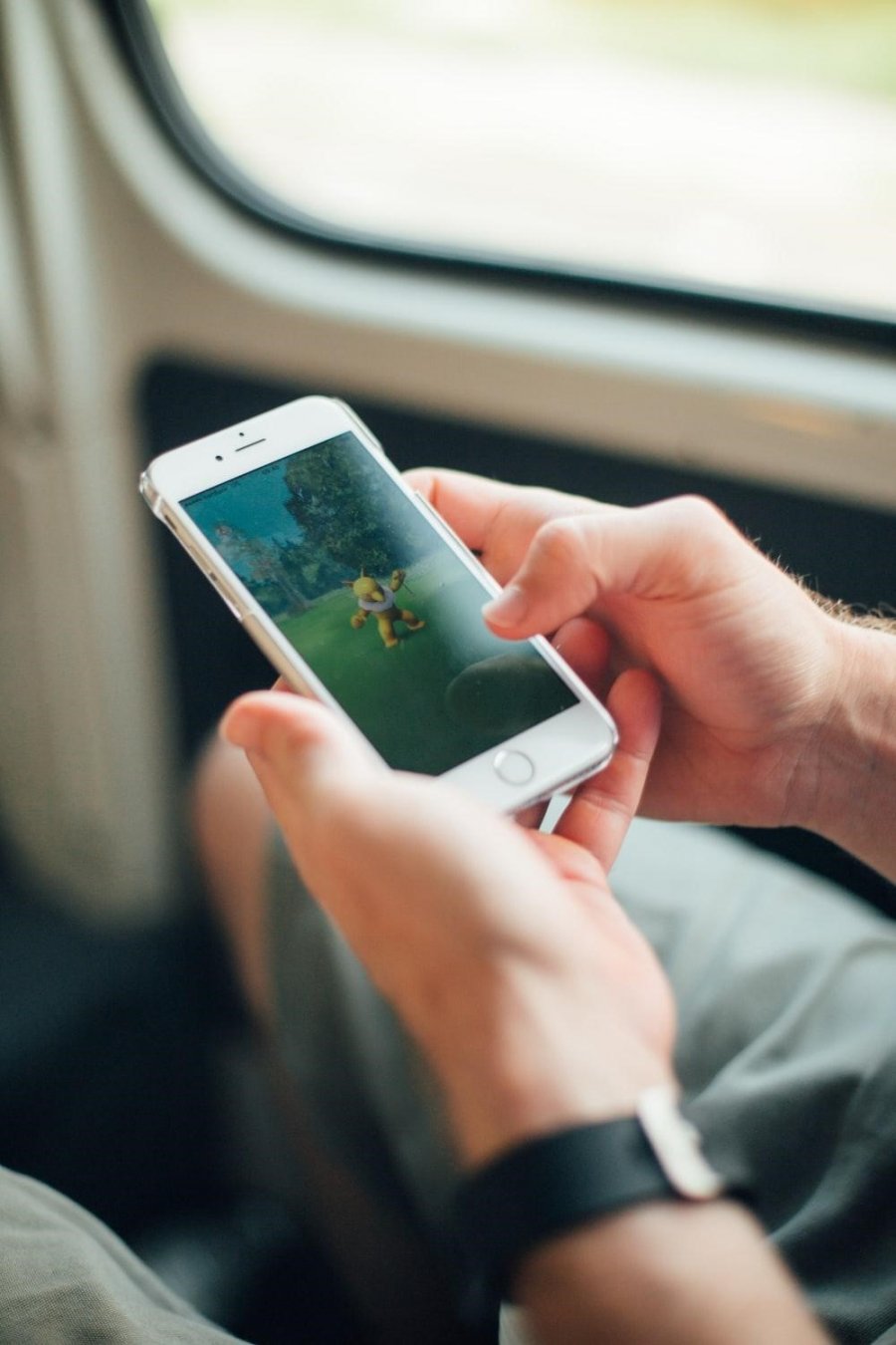 Zwei Hände halten ein Smartphone. Mit einem Daumen wird auf das Display getippt. Auf dem Display ist das Spiel Pokémon Go! zu sehen, das ein gelbes Monster anzeigt.